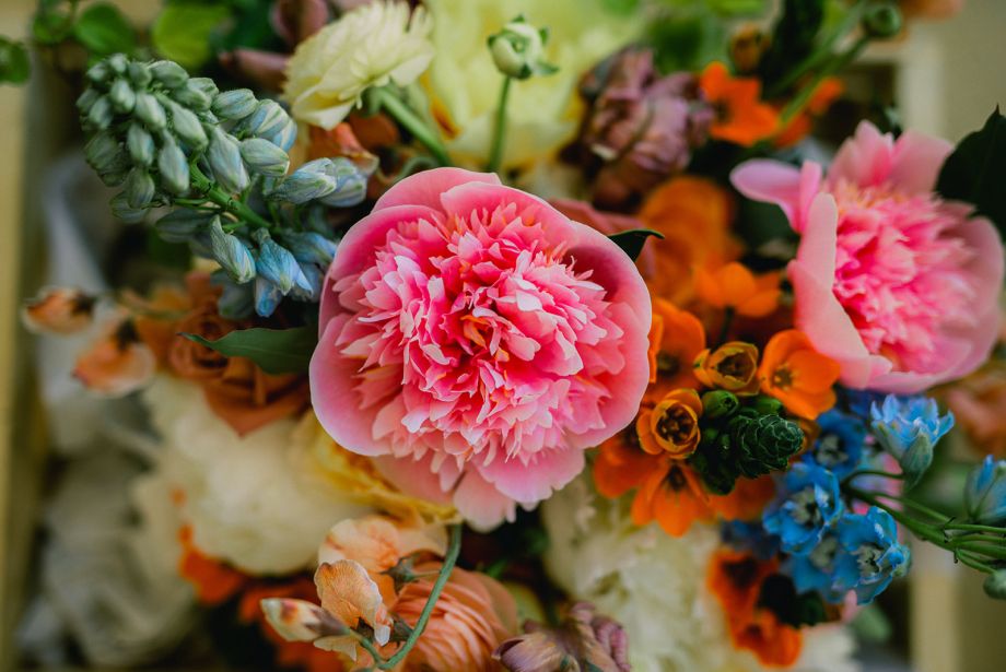Close-up of a colorful wedding bouquet with pink peonies, orange blooms, and blue accents at Wishwell House