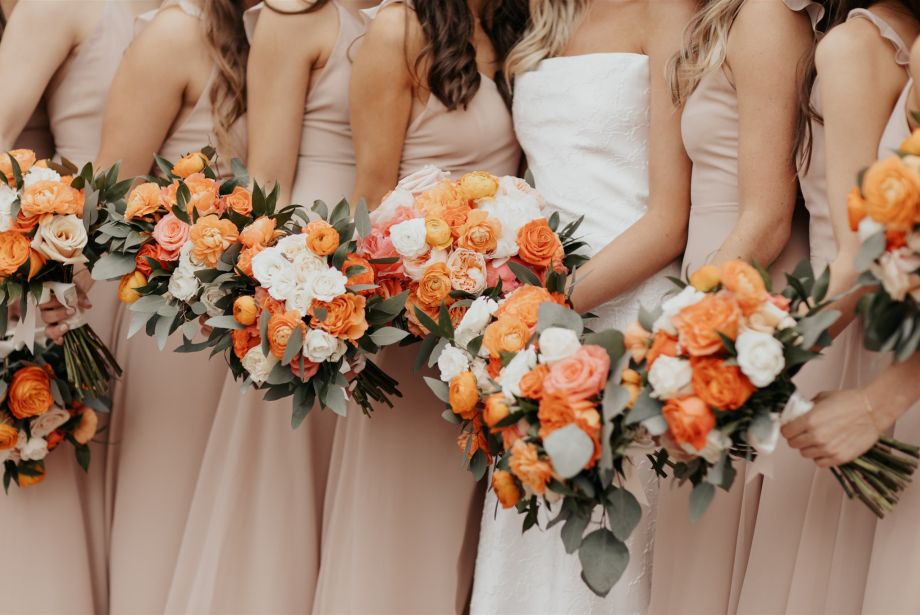 Bride and bridesmaids holding orange, peach and white rose bouquets in blush dresses at Villa Antonia wedding